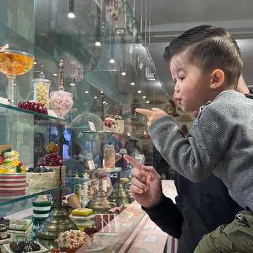 Vader draagt zijn jonge zoon terwijl ze samen door het glazen vitrine kijken naar kleurrijke nep-toetjes tijdens de tentoonstelling Grand Dessert – De geschiedenis van het toetje in Kunstmuseum Den Haag.