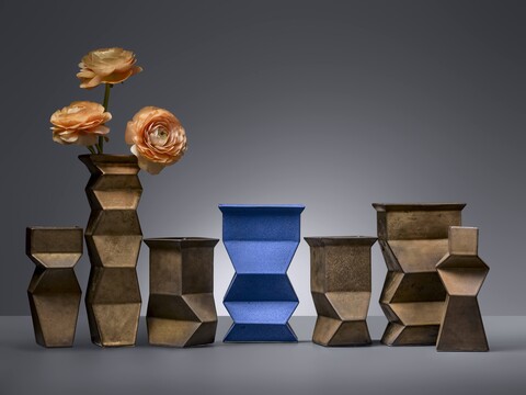 Geometrische bronzen vazen van Jan van der Vaart, met in het midden een opvallende blauwe vaas en links twee oranje bloemen als kleurrijk accent.