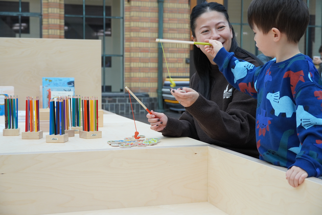 Moeder en kind vissen samen met speelgoedhengels bij het Doe-eiland